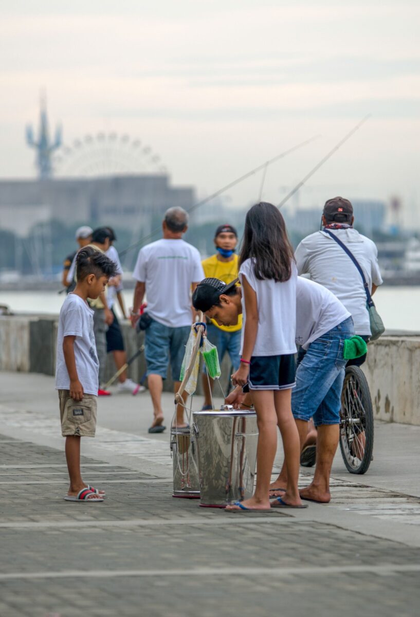 Vendors selling taho to passersby along the Baywalk in Manila during a lively afternoon.